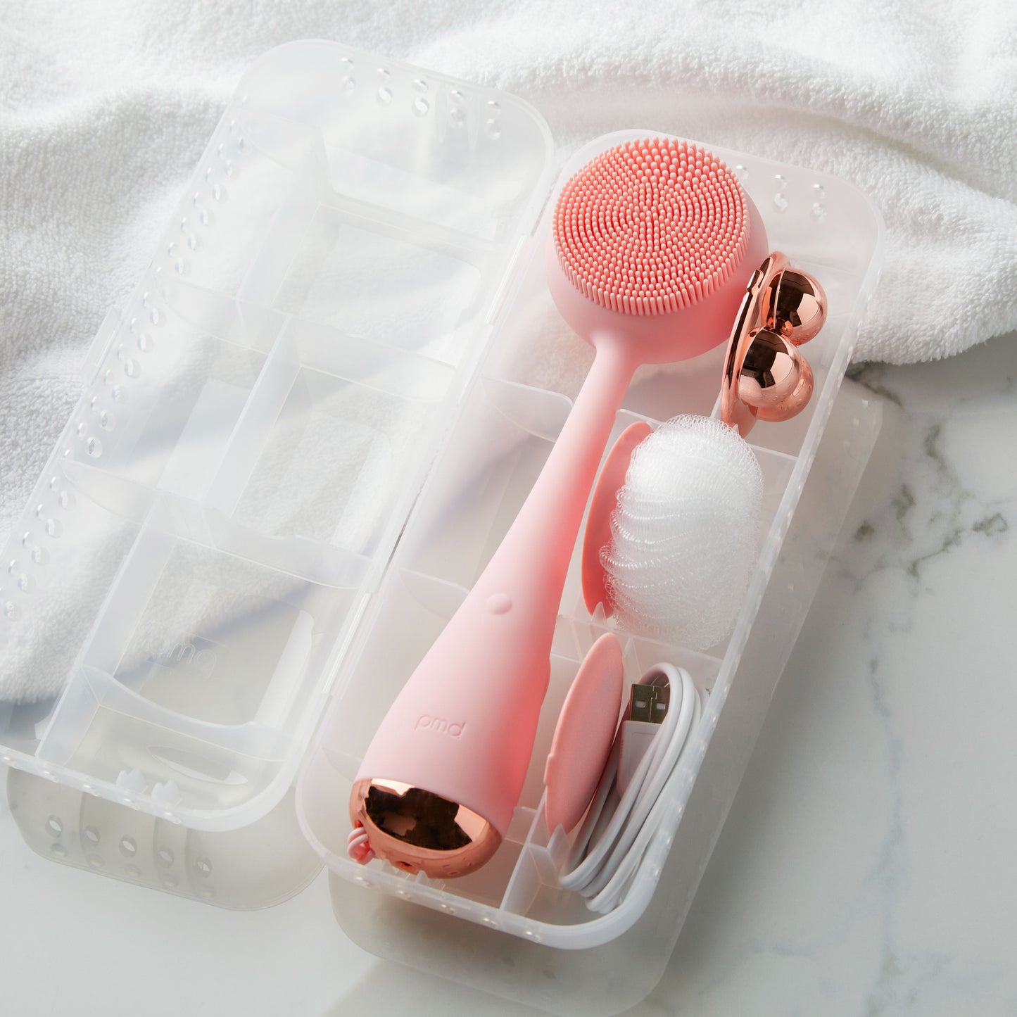 4003-Case?PMD Clean Body Case next to towel with blush PMD Clean Body and accessories inside