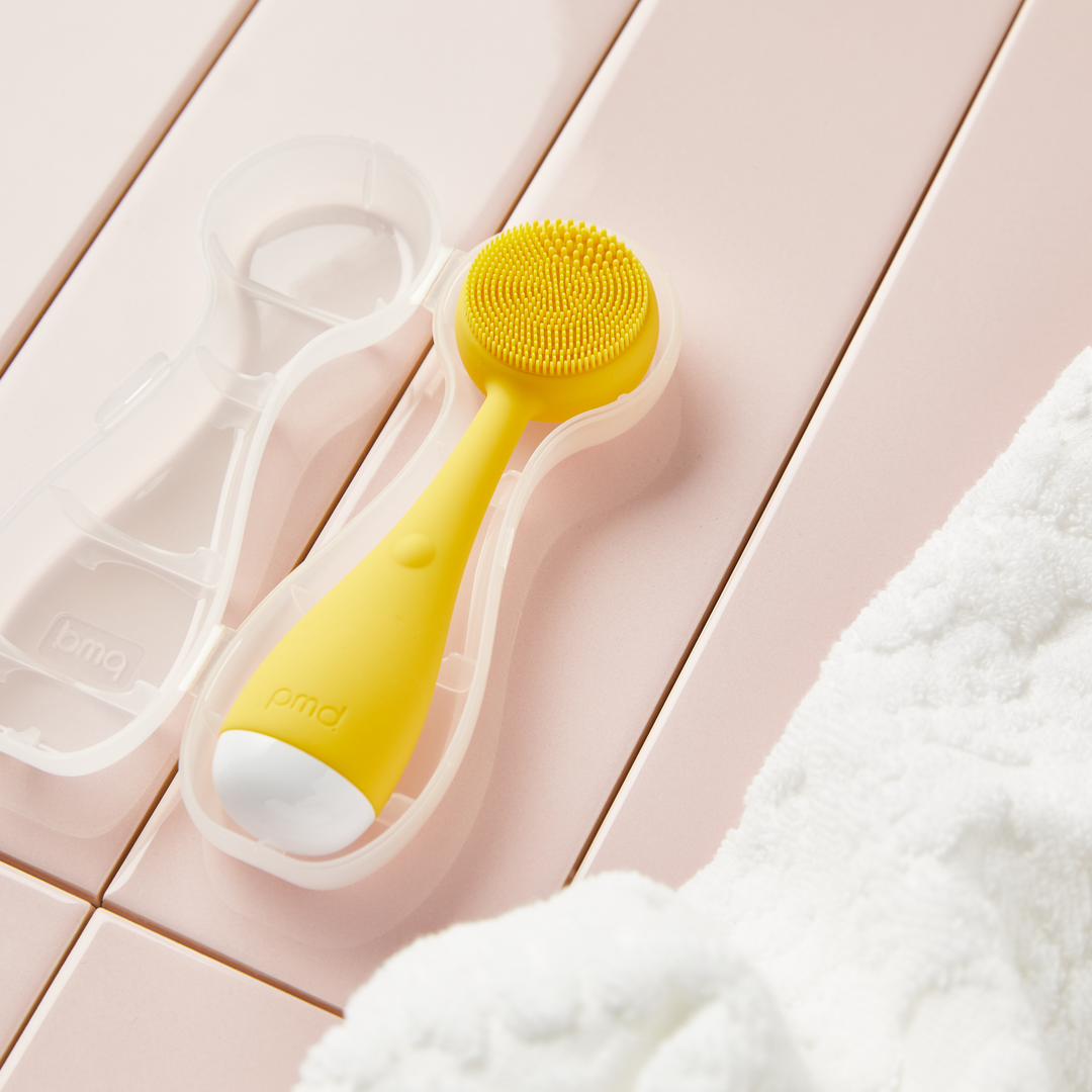 4000-CASE?PMD Clean Mini storage case with yellow PMD Clean Mini inside laying on pink tile with white towel on the side